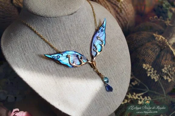 Collier pendentif branche doree avec deux ailes bleues violettes et perle bleue, presente sur buste