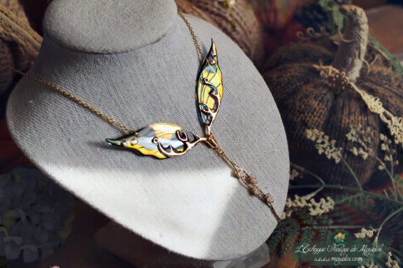 Collier pendentif branche doree avec deux ailes jaunes dorees, presente sur buste porte-bijoux