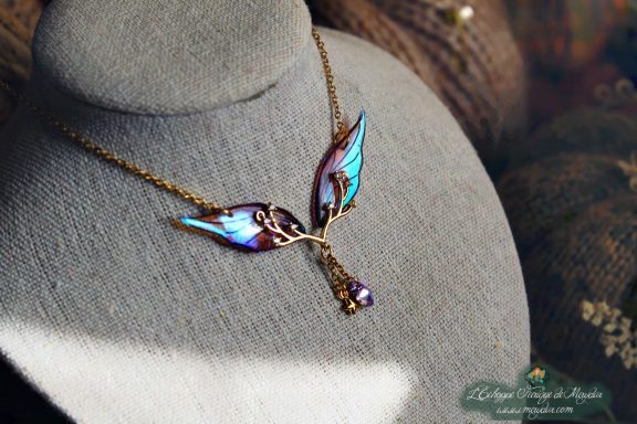 Collier pendentif branche doree avec deux ailes bleues et perles, presente sur buste porte-bijoux
