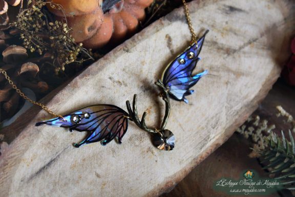 Collier pendentif bois de cerf avec deux ailes turquoise violettes et perle violette, presente sur bois