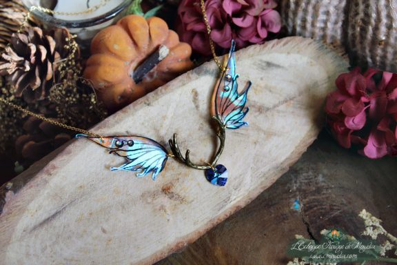 Collier pendentif bois de cerf avec aile bleue orange et perle coeur bleue, presente sur bois