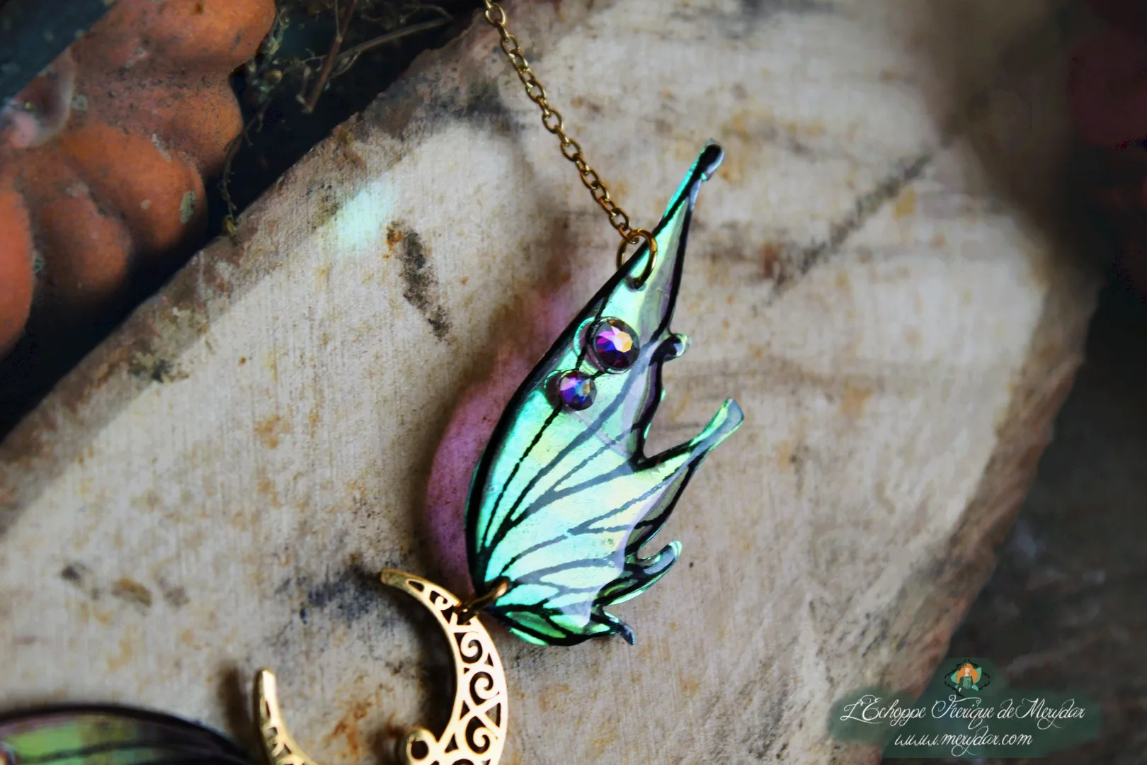 Collier pendentif aile turquoise violette avec breloque lune, vue rapprochee sur bois