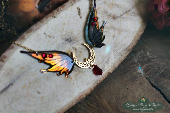 Collier pendentif aile orange jaune avec breloque lune et pierre rouge, gros plan sur bois