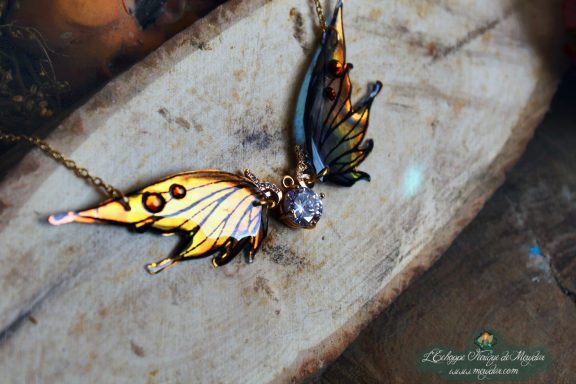 Collier pendentif aile jaune avec breloque lune et pierre transparente, gros plan sur bois