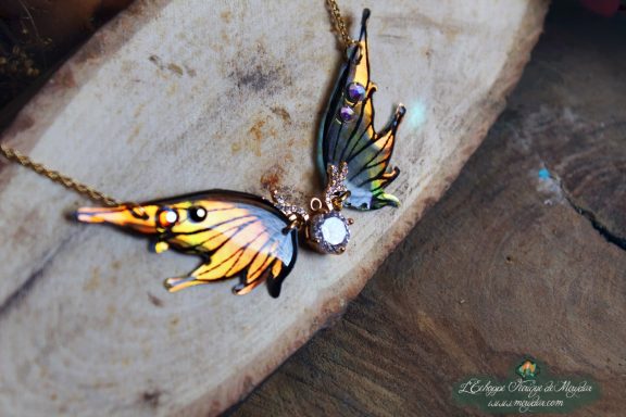 Collier pendentif aile orange jaune avec breloque lune et pierre, gros plan sur bois