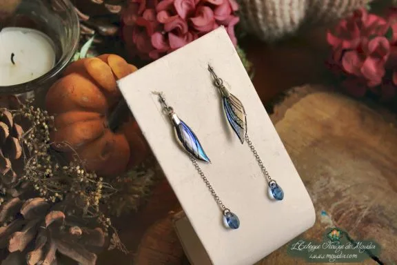 Boucles d'oreilles longues aile bleue avec perle bleue, presentees sur socle