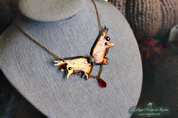 Collier pendentif renard aile orange avec perle rouge, presente sur buste porte-bijoux