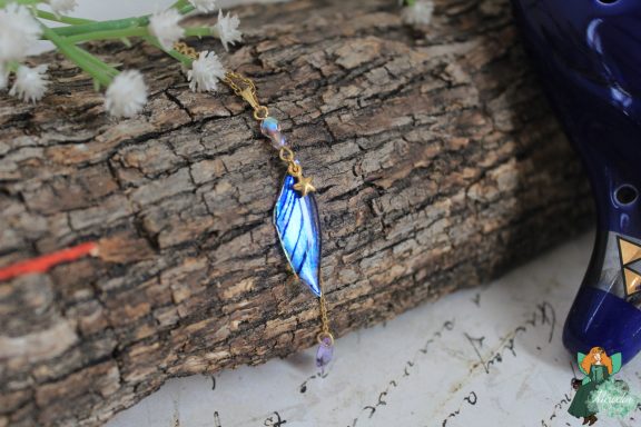 Pendentif aile feuille bleue sur chaine doree, presente sur ecorce