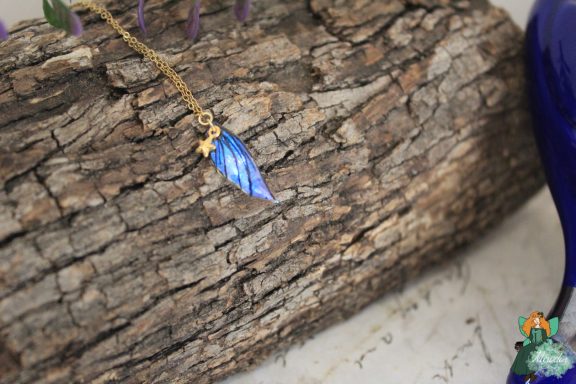 Petit pendentif aile feuille bleue sur chaine, presente sur ecorce