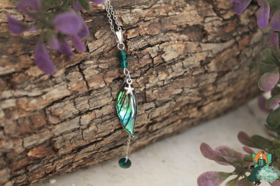 Pendentif aile plume verte avec breloque etoile, presente sur ecorce
