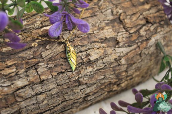 Pendentif aile plume jaune sur chaine doree, presente sur ecorce