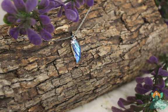 Petit pendentif aile plume bleue sur chaine, presente sur ecorce