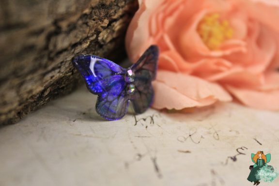 Petite broche papillon bleu violet, presentee sur fleur rose