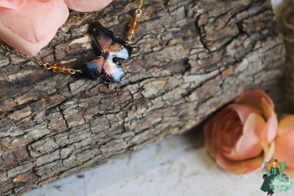 Pendentif papillon blanc bleu avec perle ambre, tenu en main