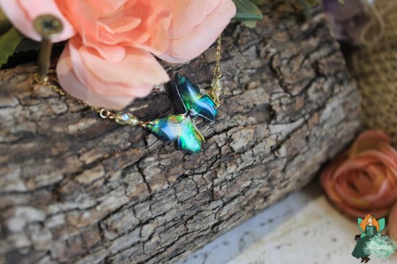 Bracelet chaine avec breloque papillon vert bleu et perles, presente sur fleur rose