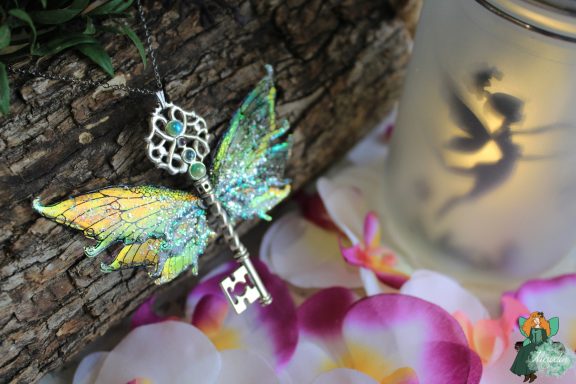 Pendentif cle ailee verte pailetee, presente sur fleurs