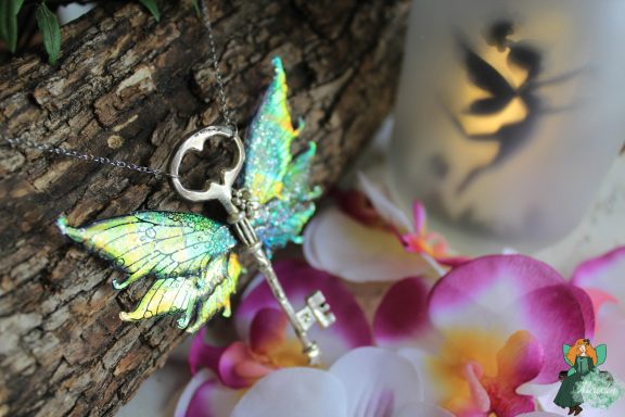 Pendentif cle ailee verte irisee, presente sur fleurs