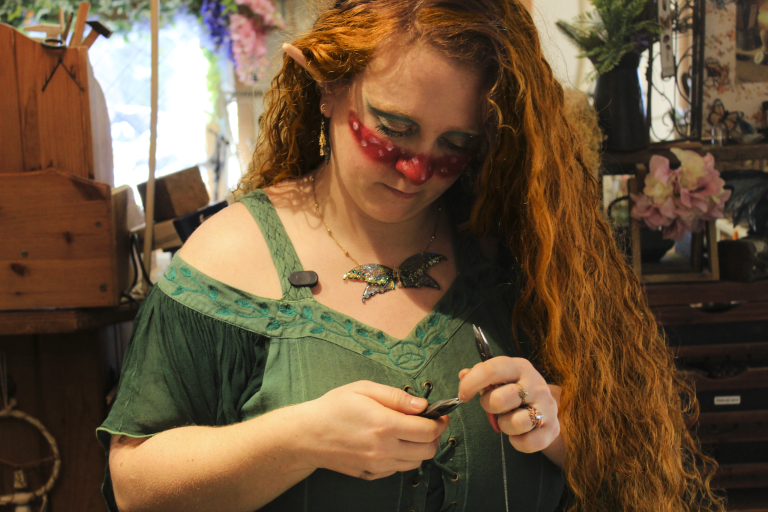 Portrait d'une femme aux cheveux roux en robe verte, en train de creer un bijou