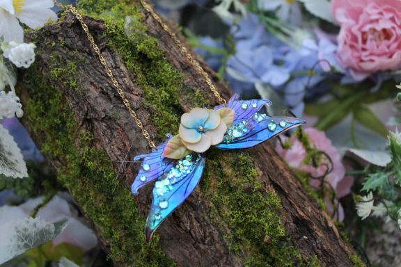 Pendentif aile de fee bleue avec fleur pale, chaine sur mousse