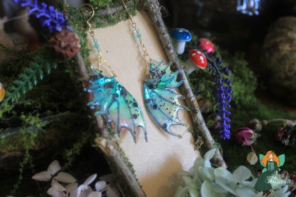 Boucles d'oreilles aile de dragon turquoise, presentees sur presentoir bois