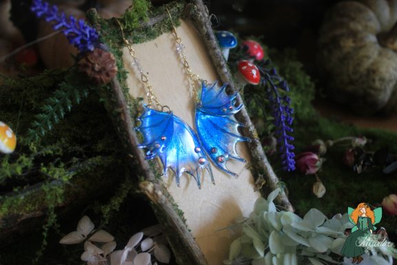 Boucles d'oreilles aile de dragon bleue, presentees sur presentoir bois