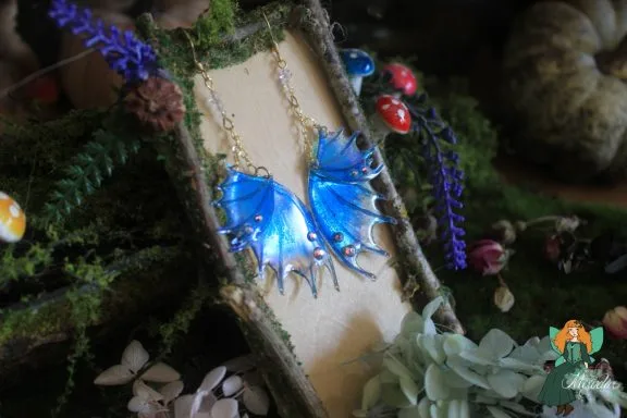 Boucles d'oreilles aile de dragon bleue, presentees sur presentoir bois